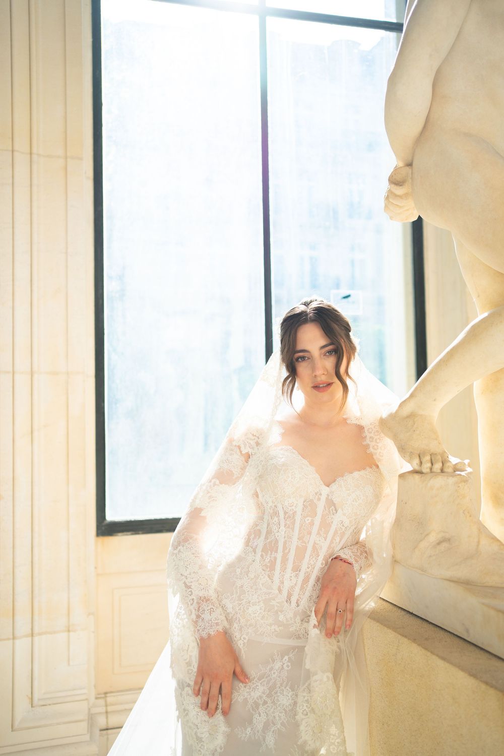 A dreamy bridal portrait in soft white lace against a window with ethereal natural light creating a romantic atmosphere.
