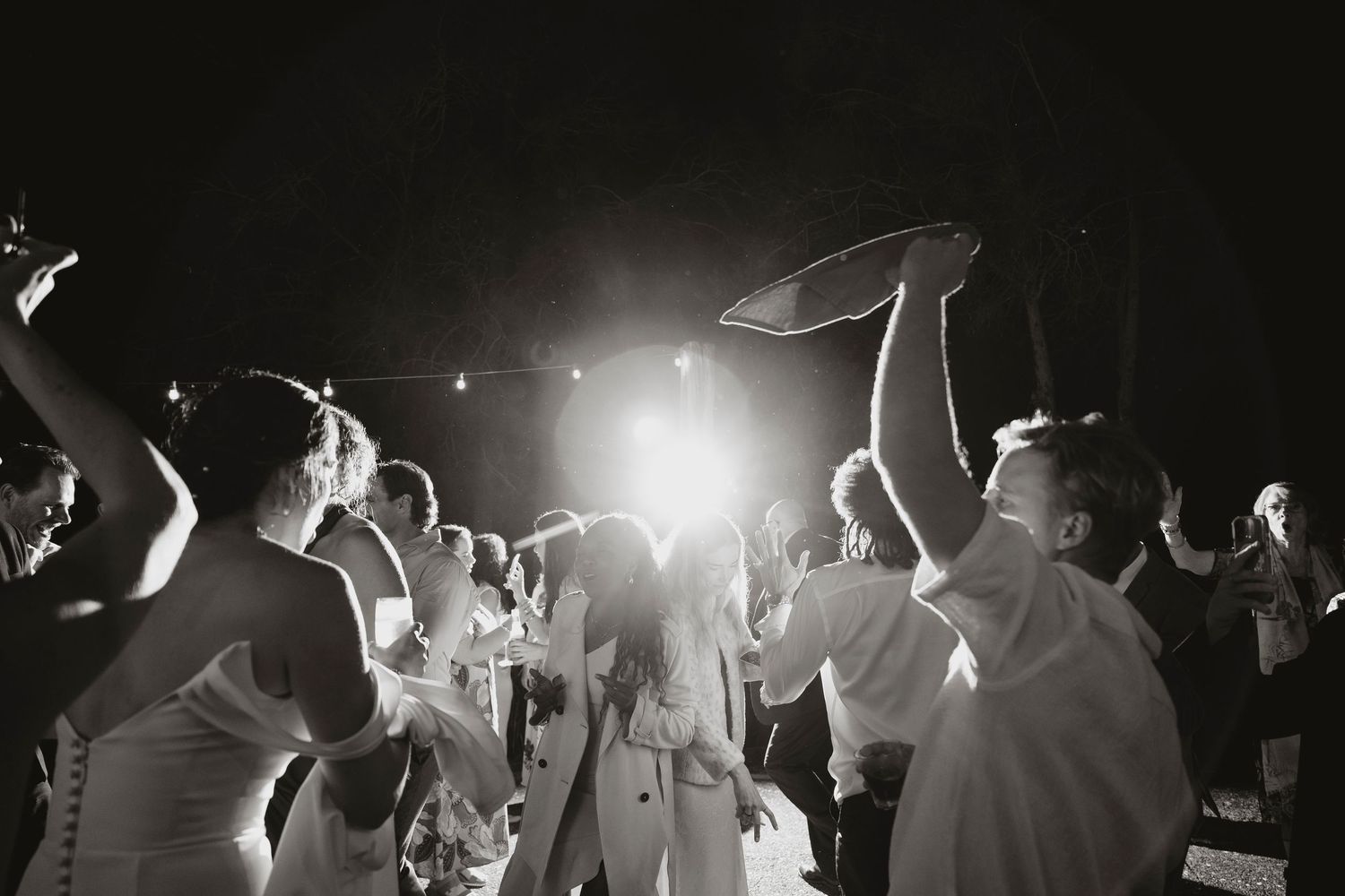 Wedding party guests dancing and celebrating energetically on a dance floor illuminated by colorful lights.