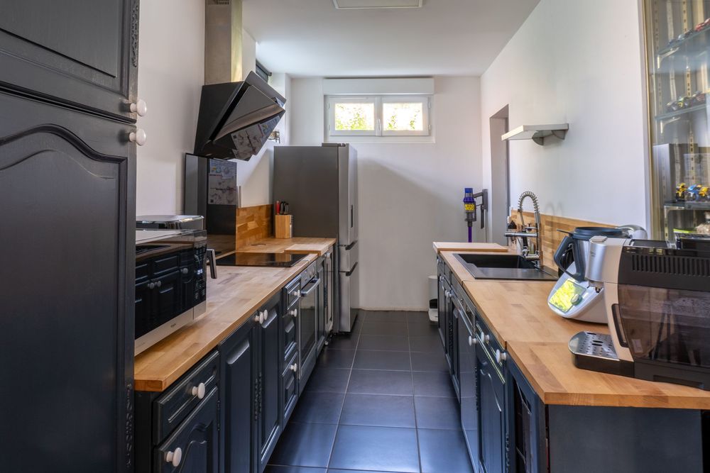 Modern galley kitchen with black cabinets, wooden countertops, and dark tile flooring in a bright, narrow space.