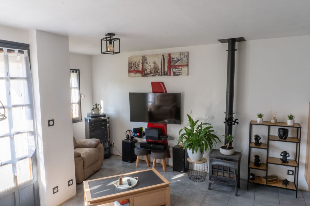 Modern living room with black wood stove, wall-mounted TV, industrial light fixture and rustic decor elements.