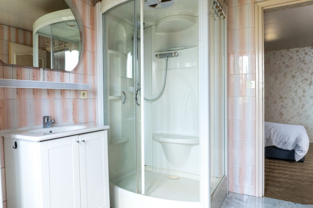 Modern bathroom interior with white vanity cabinet, glass shower enclosure, and pink striped wallpaper.
