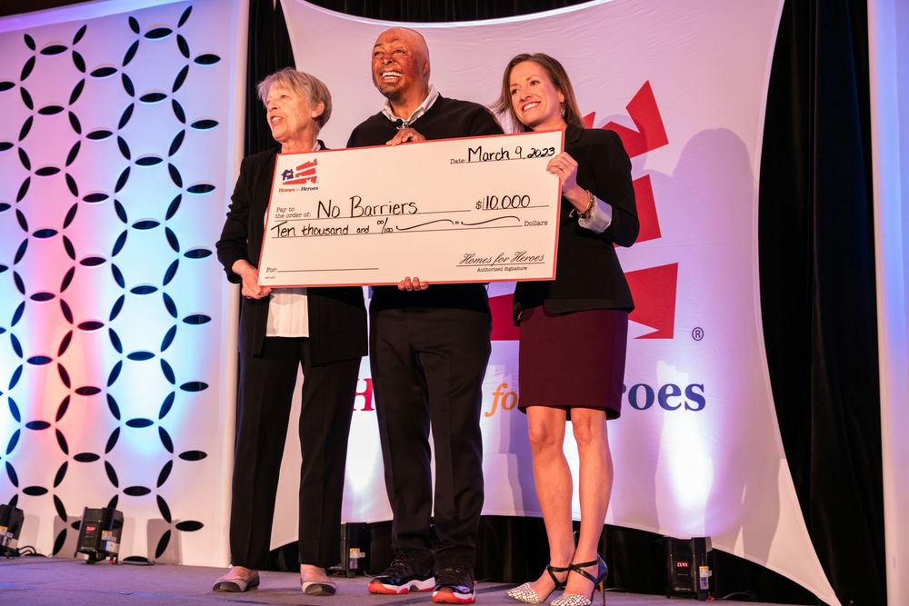 Several people stand on stage holding a large presentation check during an awards ceremony with purple lighting.