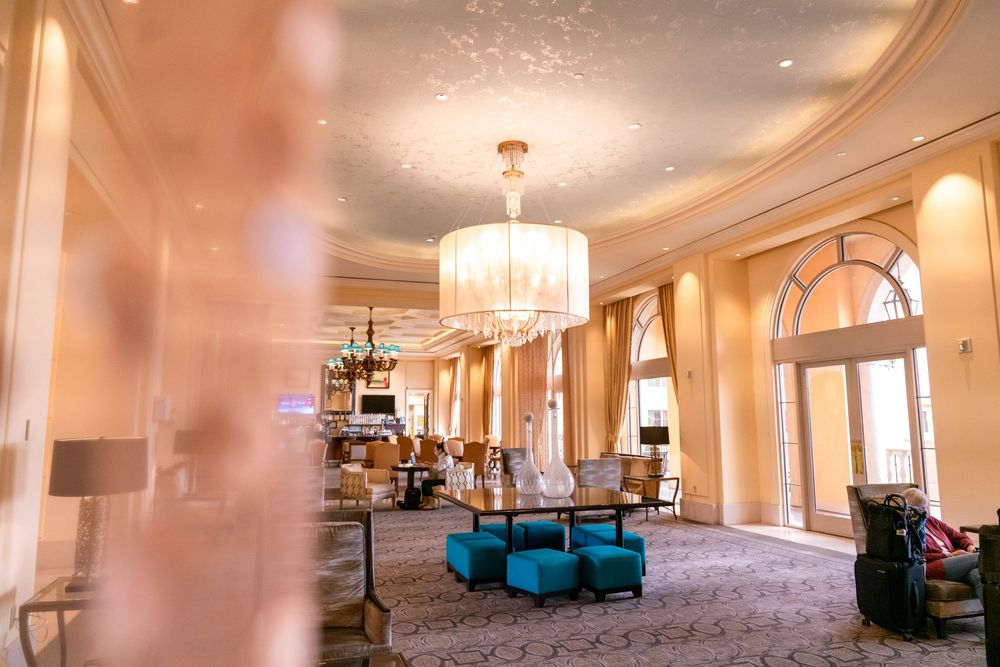A panoramic view of an elegant ballroom interior with crystal chandeliers, warm lighting, and plush turquoise seating areas.