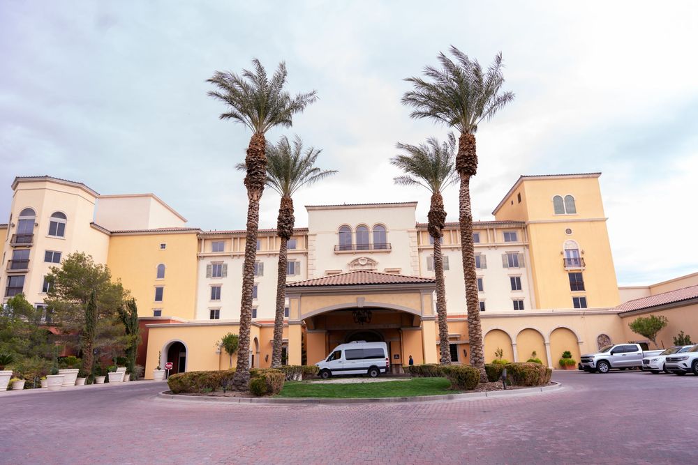 Modern Mediterranean-style apartment buildings with palm trees and arched architecture line a residential complex driveway.