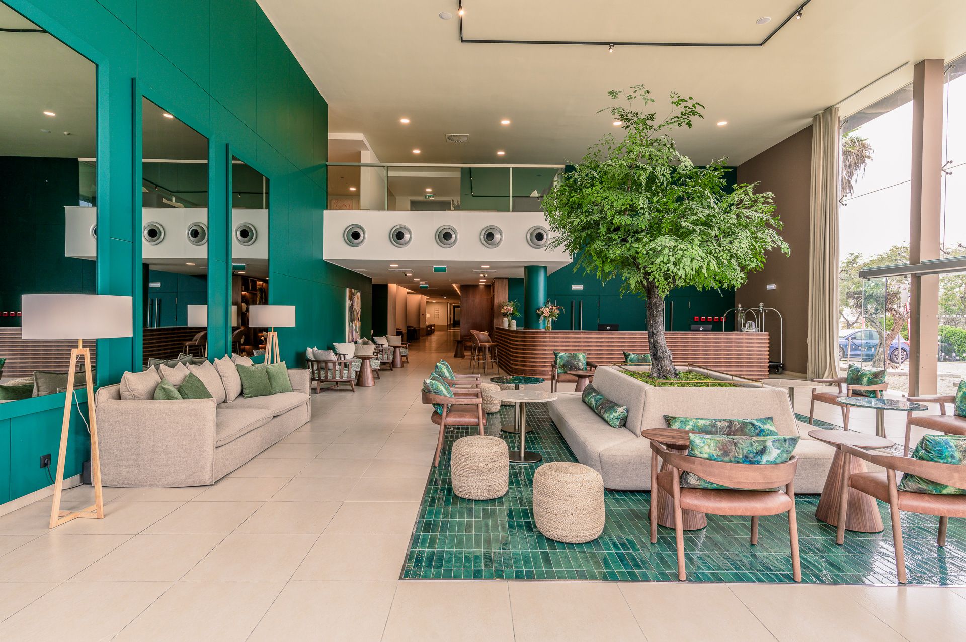 Stylish lounge space of a hotel in the Algarve, with teal walls, wooden furniture, and abundant natural lighting by Parallel Studios