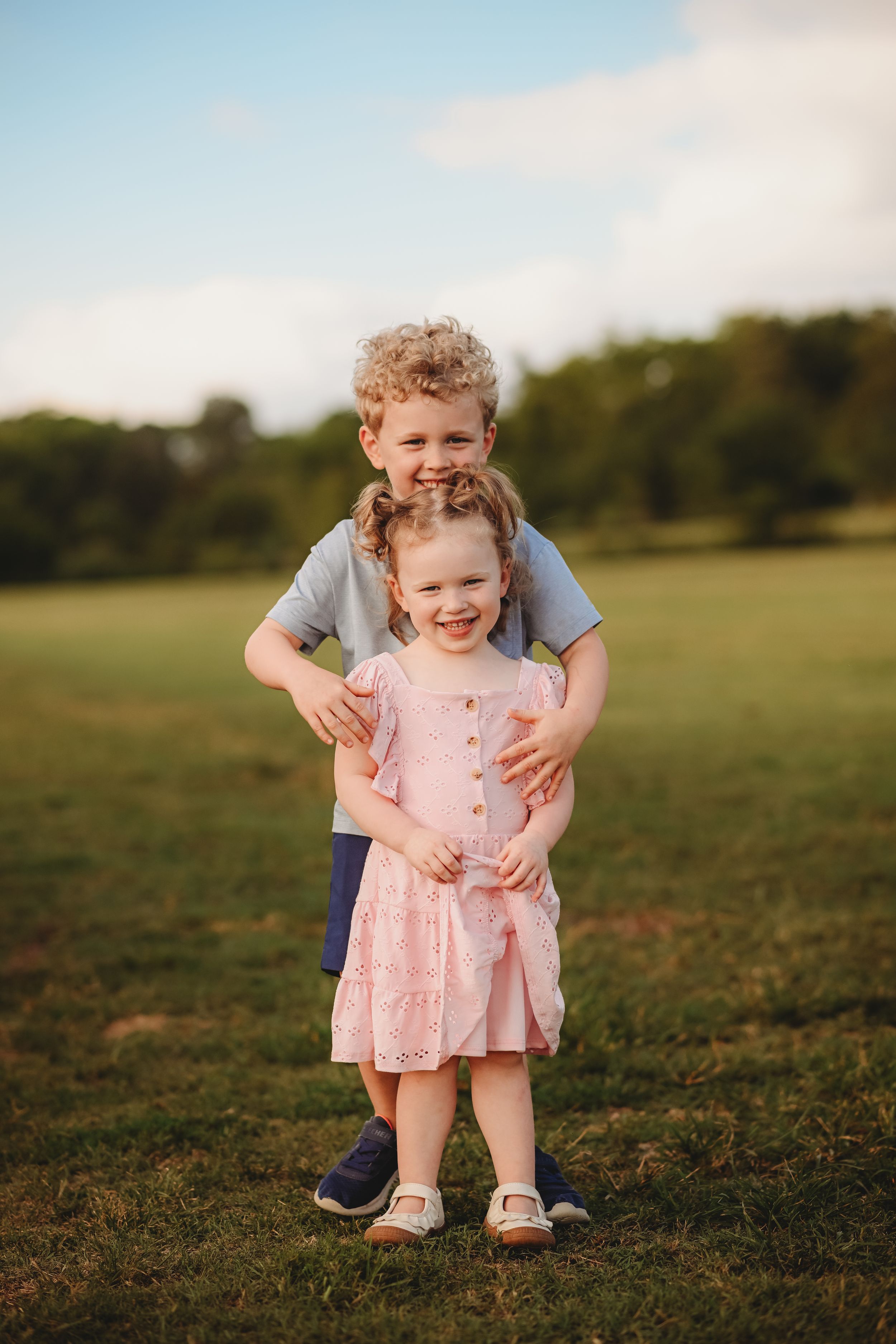A tender moment captured in golden light as someone steadies a toddler in a pink dress.