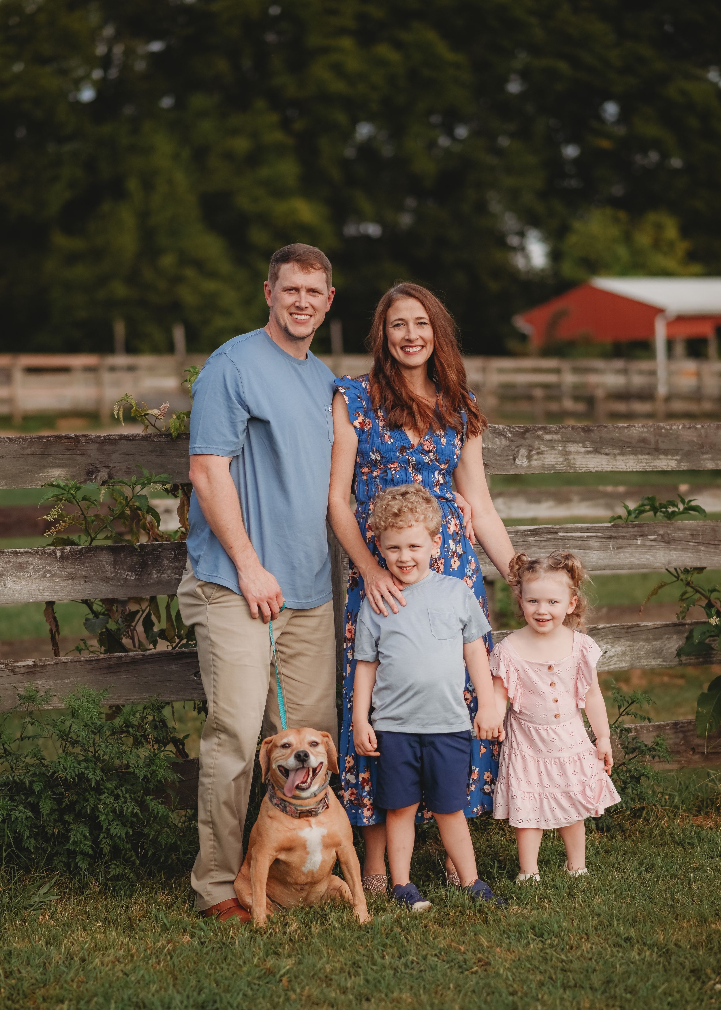 Family and their golden retriever pose together by a rustic wooden fence at sunset.
