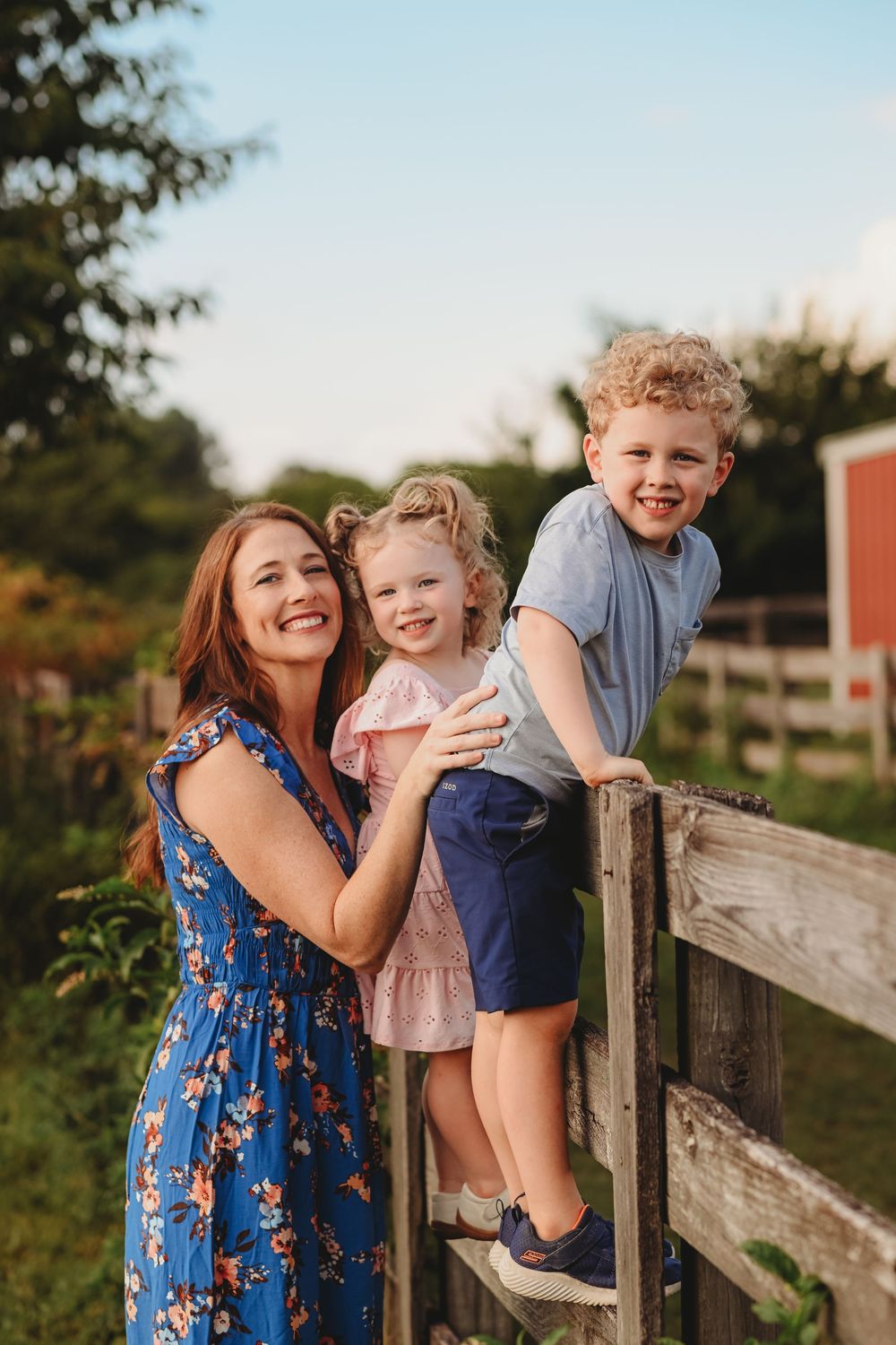 Playful family moment captured by a wooden fence with a red barn visible in the distance.