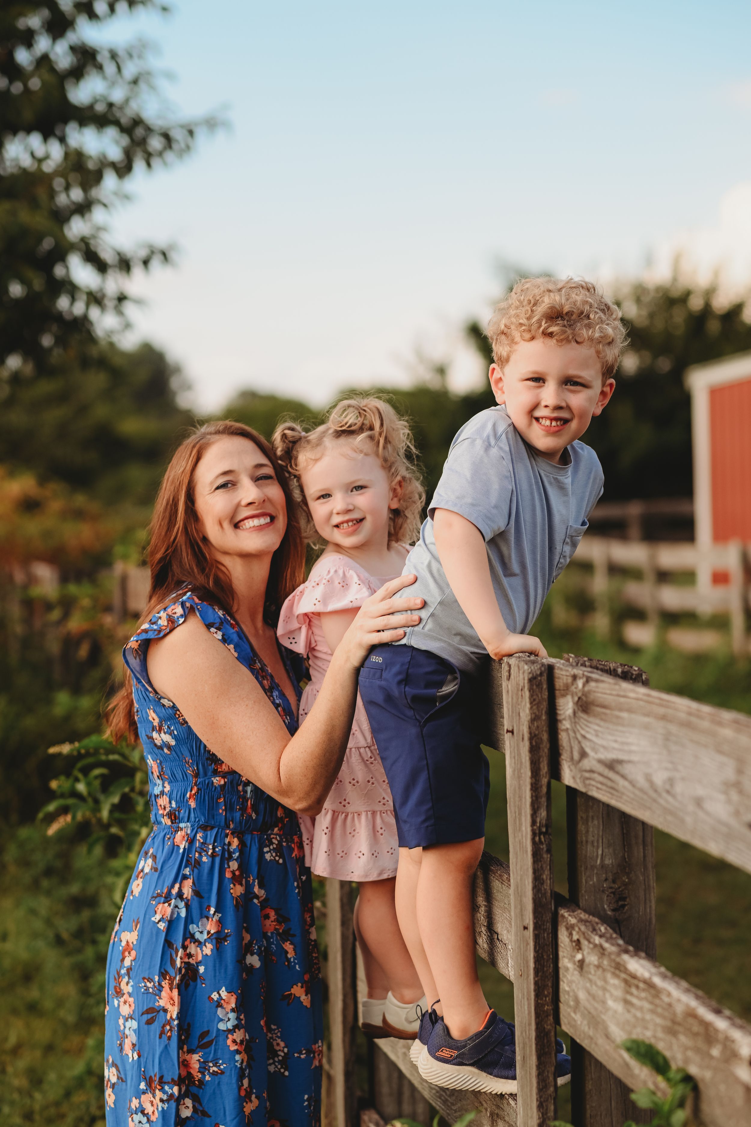 Playful family moment captured by a wooden fence with a red barn visible in the distance.