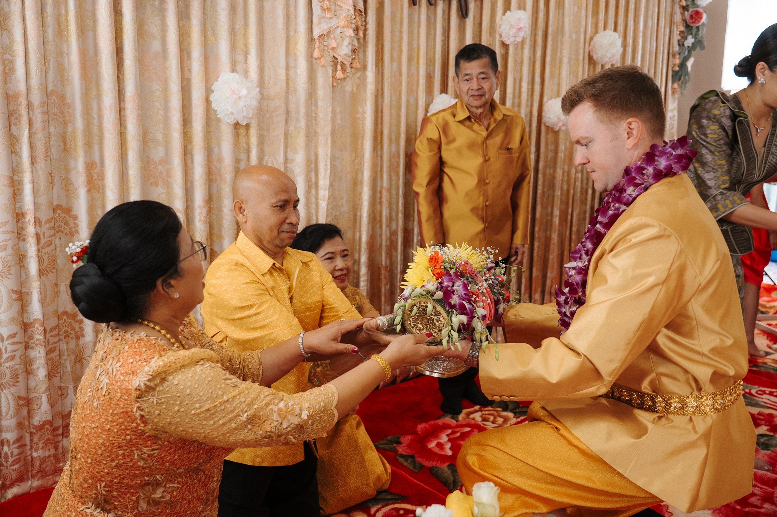 A group of people wearing gold attire exchange flower garlands during a traditional cultural ceremony.