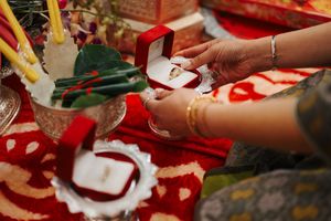 Close-up of traditional ceremony items and offerings arranged on red fabric with decorative patterns.