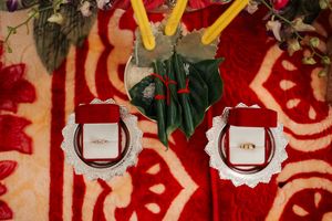 Two decorative wedding rings displayed on white scalloped plates against a red and white patterned background.