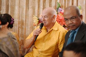 Guests gathered at formal event with speaker in yellow shirt holding microphone during celebration.