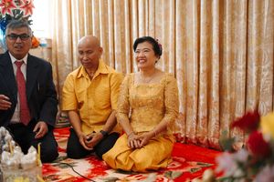 Traditional celebration gathering with people seated along a table against curtained backdrop.