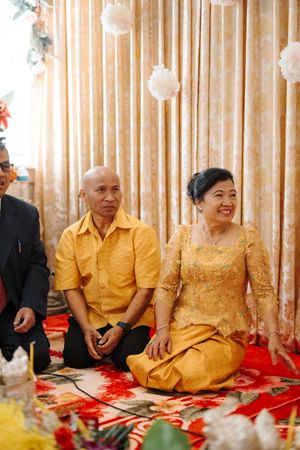 People in yellow outfits sitting on red carpets during what appears to be a traditional celebration or ceremony.