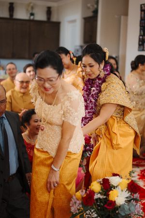 Traditional Thai wedding ceremony with guests wearing yellow and gold silk outfits and purple floral garlands.