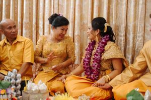 People wearing traditional yellow and gold attire gather at a cultural celebration with floral garlands and decorations.