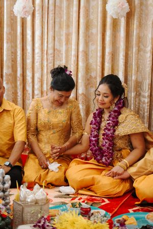 People wearing traditional yellow and red attire sit together during a cultural ceremony with flower garlands and offerings.