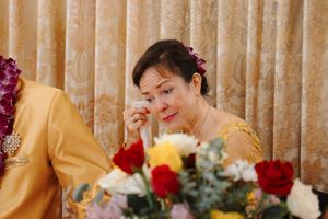 People sitting at a long wedding reception table decorated with red and yellow floral centerpieces and candles.