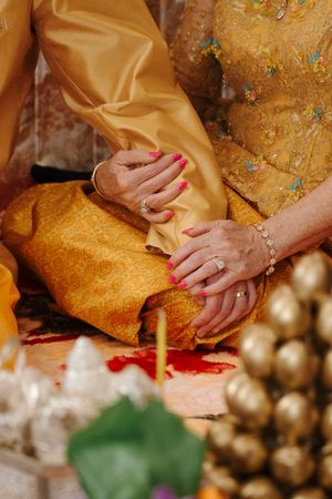 Close-up of hands resting on traditional gold and yellow fabric with decorative details.