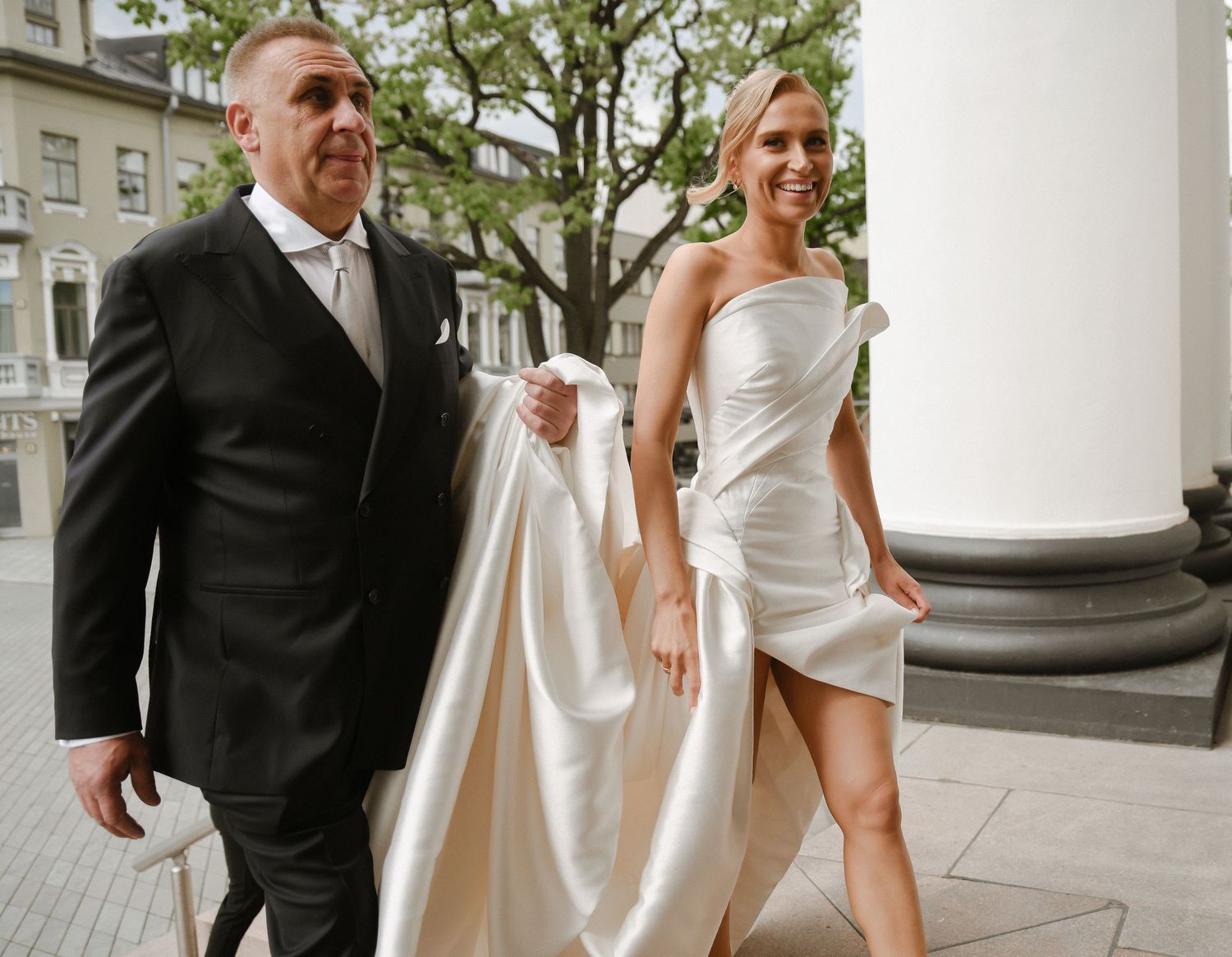 Wedding party walking outside between white columns on building exterior.