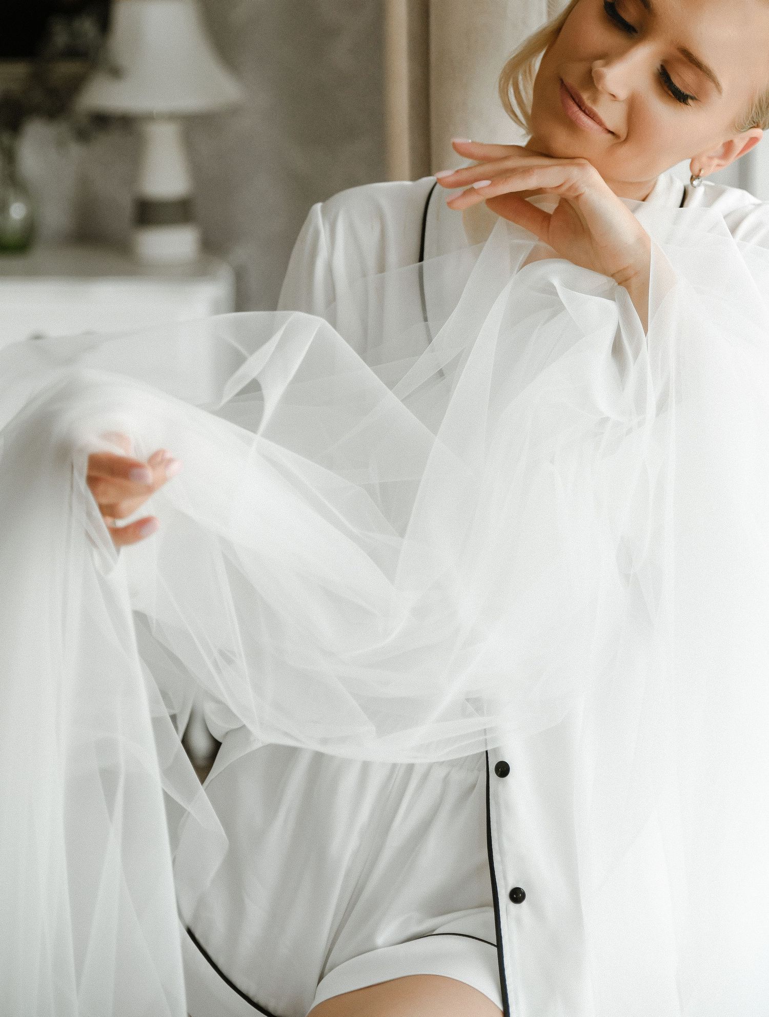 A dreamy bridal boudoir scene with flowing white tulle fabric and silk robe in a soft, ethereal setting.