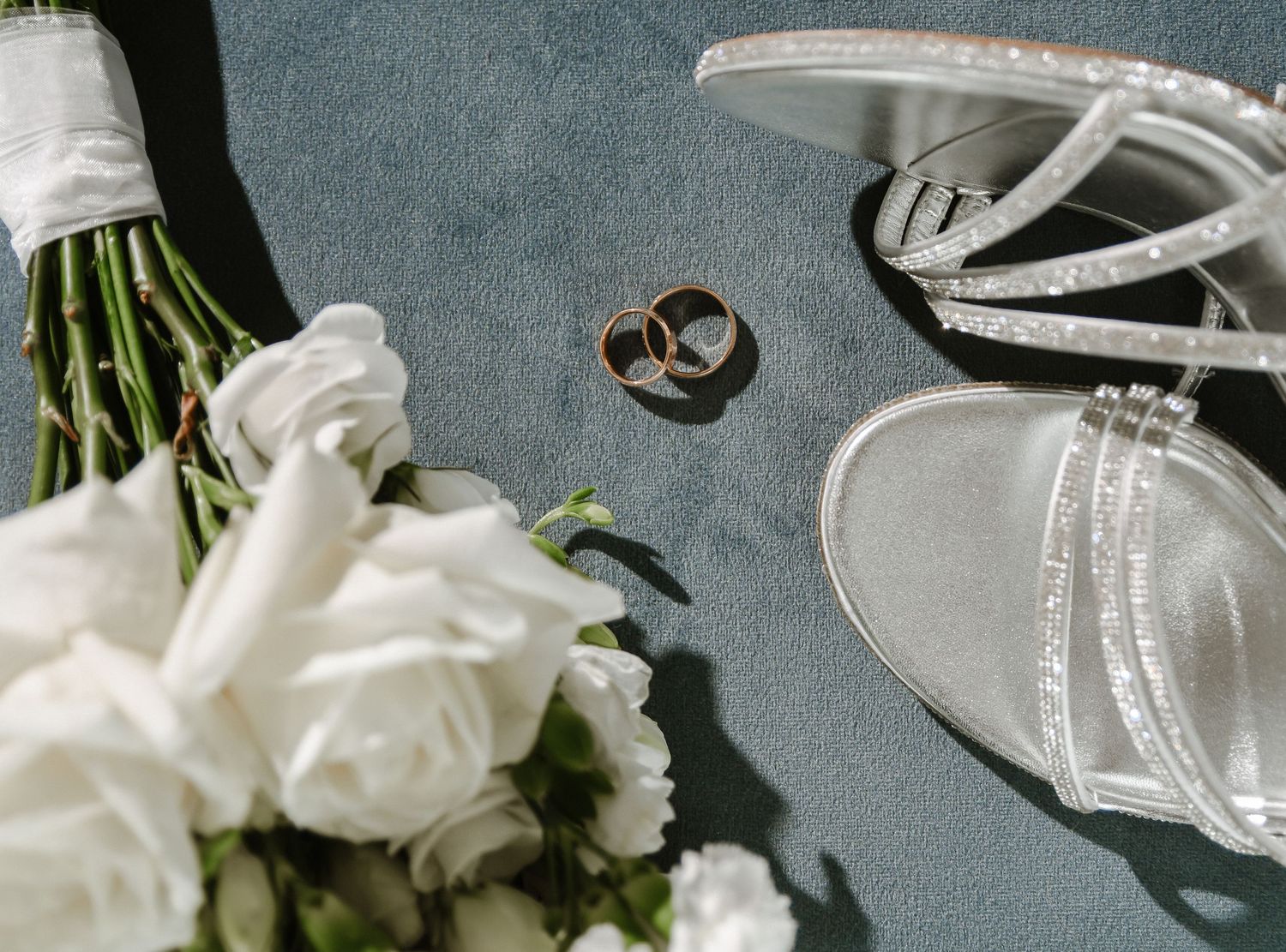 Wedding details with white roses and elegant rings arranged on a gray background.
