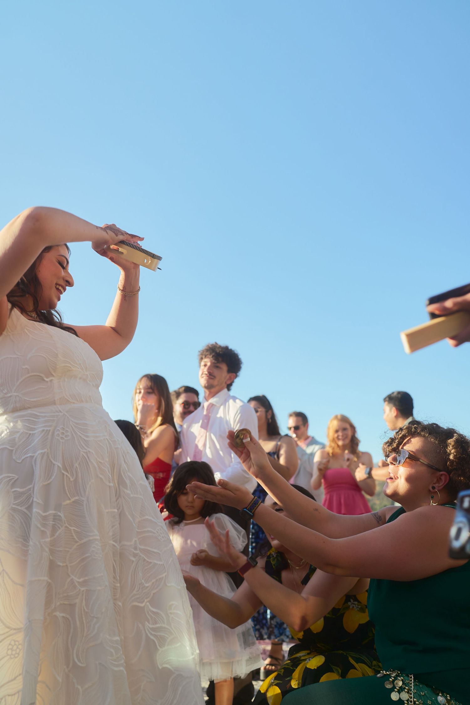 Wedding photography shot of a bride in white lace gown dancing with guests outdoors under clear blue sky at wedding celebration in Napa.