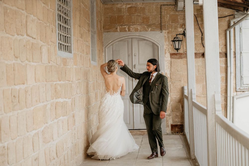 Elegant wedding couple strolls through a bright stone hallway with arched windows in a historic building.