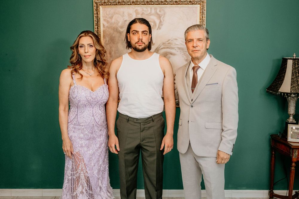 A formal group photo with three people standing against a green wall with a framed picture and lamp.