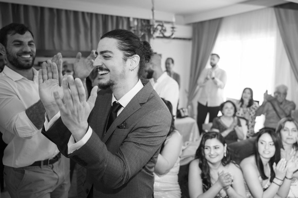 Black and white photo showing joyful celebration at a gathering with people clapping and smiling in a room.