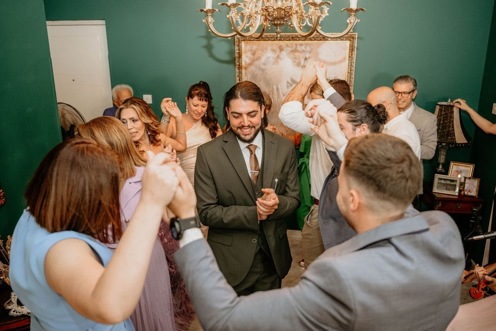 A celebratory gathering with people dancing and enjoying themselves in a room with green walls and ornate decor.
