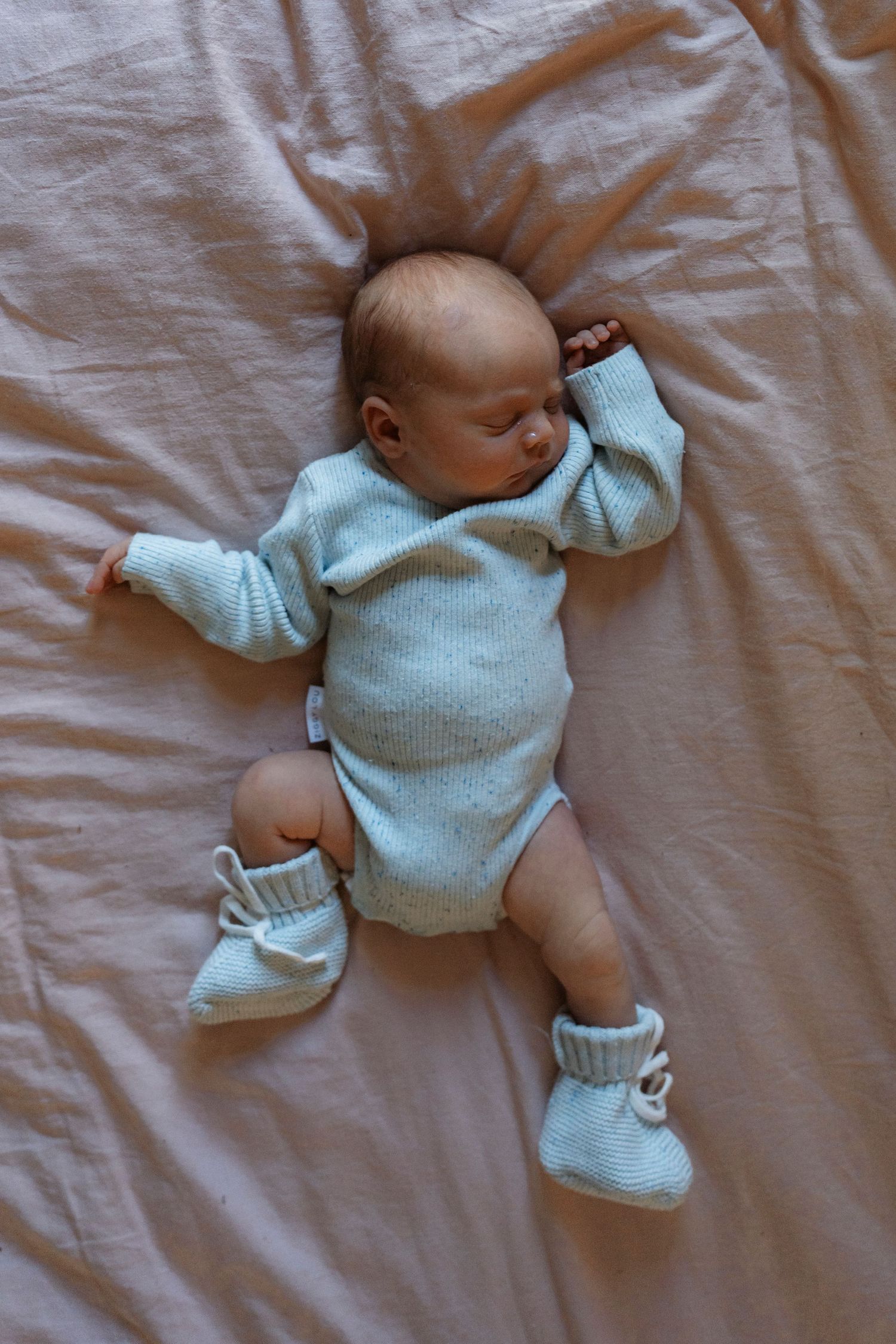 Small infant wearing cozy mint green sweater and booties lying on soft pink bedding in four peaceful sleeping poses.