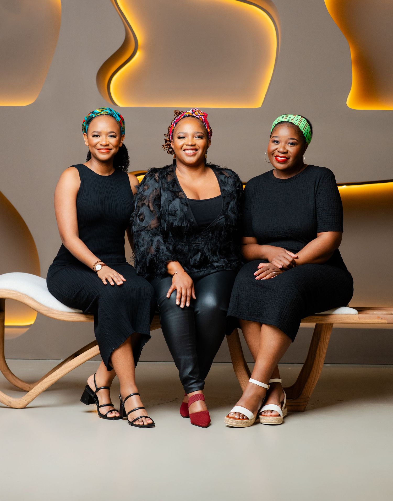 Three people in black outfits sitting together with focus on their stylish sandals and footwear.