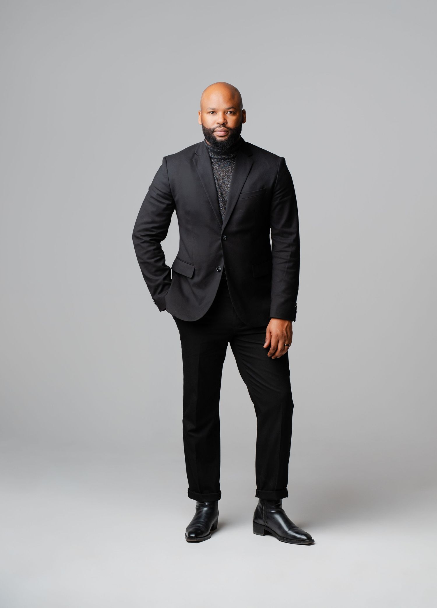 Professional studio portrait series showing a person in an all-black suit ensemble against a light gray backdrop.