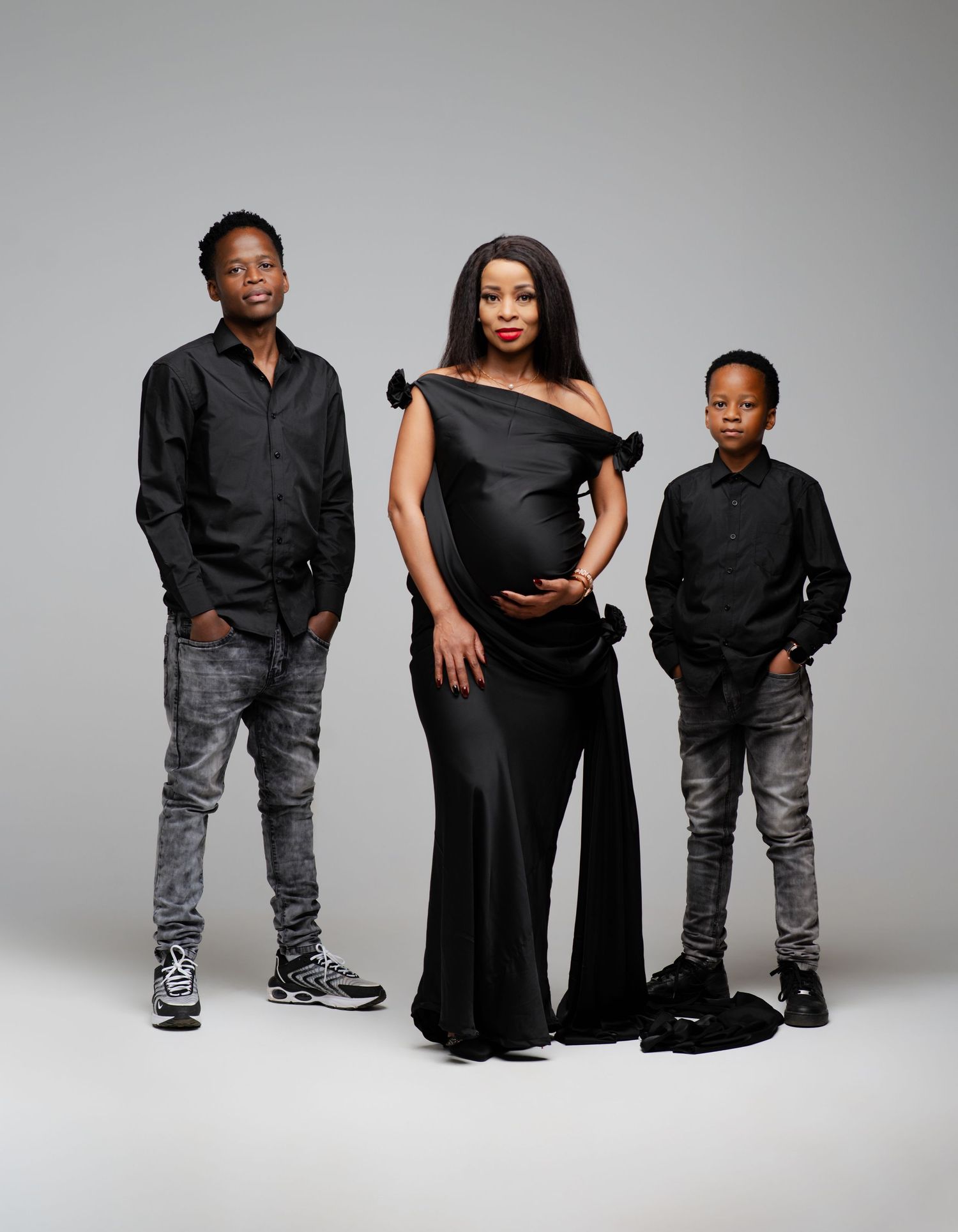Studio fashion portrait showing coordinated family in black tops and distressed jeans against white backdrop.