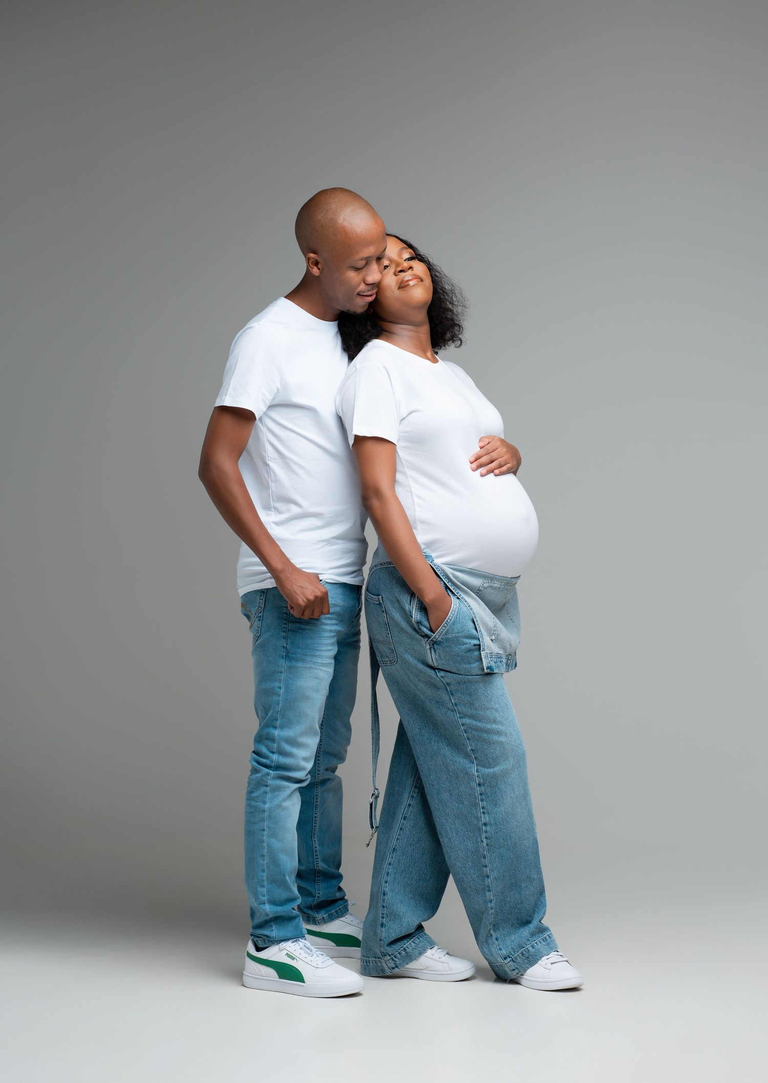 Two people in matching white shirts and blue jeans pose playfully in a sequence of casual studio shots against a gray backdrop.