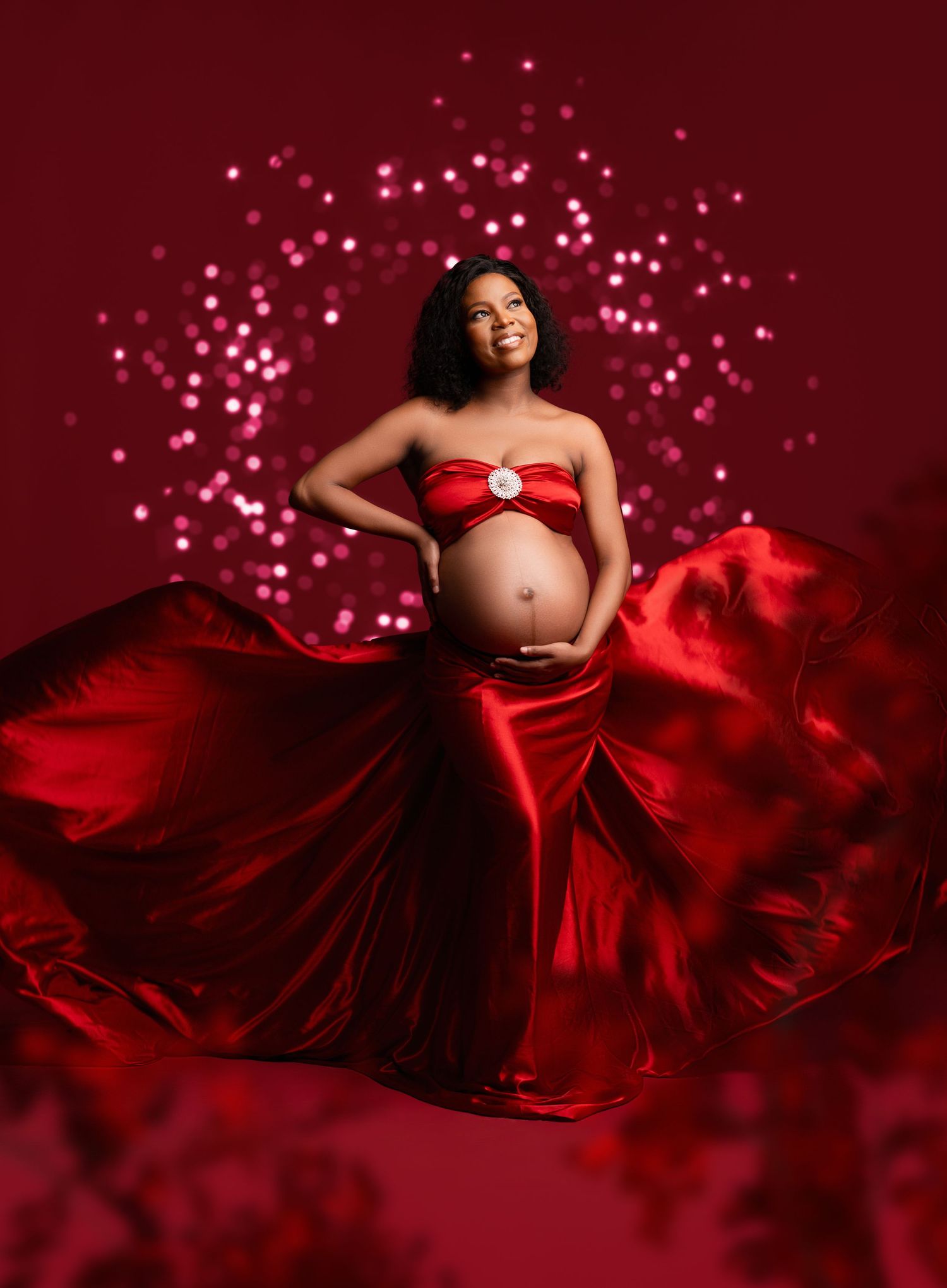 A maternity photo series in deep red featuring flowing fabric and sparkling bokeh lights against a burgundy backdrop.