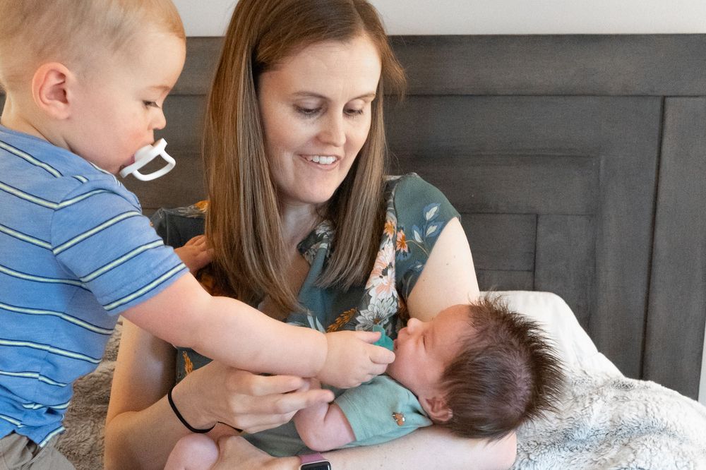 Two people share a tender moment with a newborn baby while sitting on a gray couch.