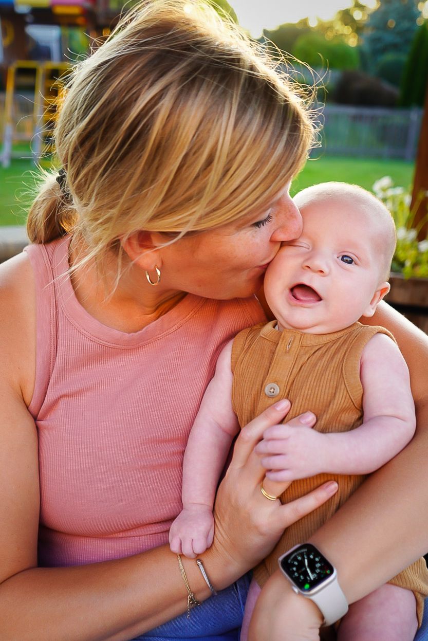 A touching outdoor moment showing a tender kiss and joyful laugh on a sunny day wearing pink and brown clothing.