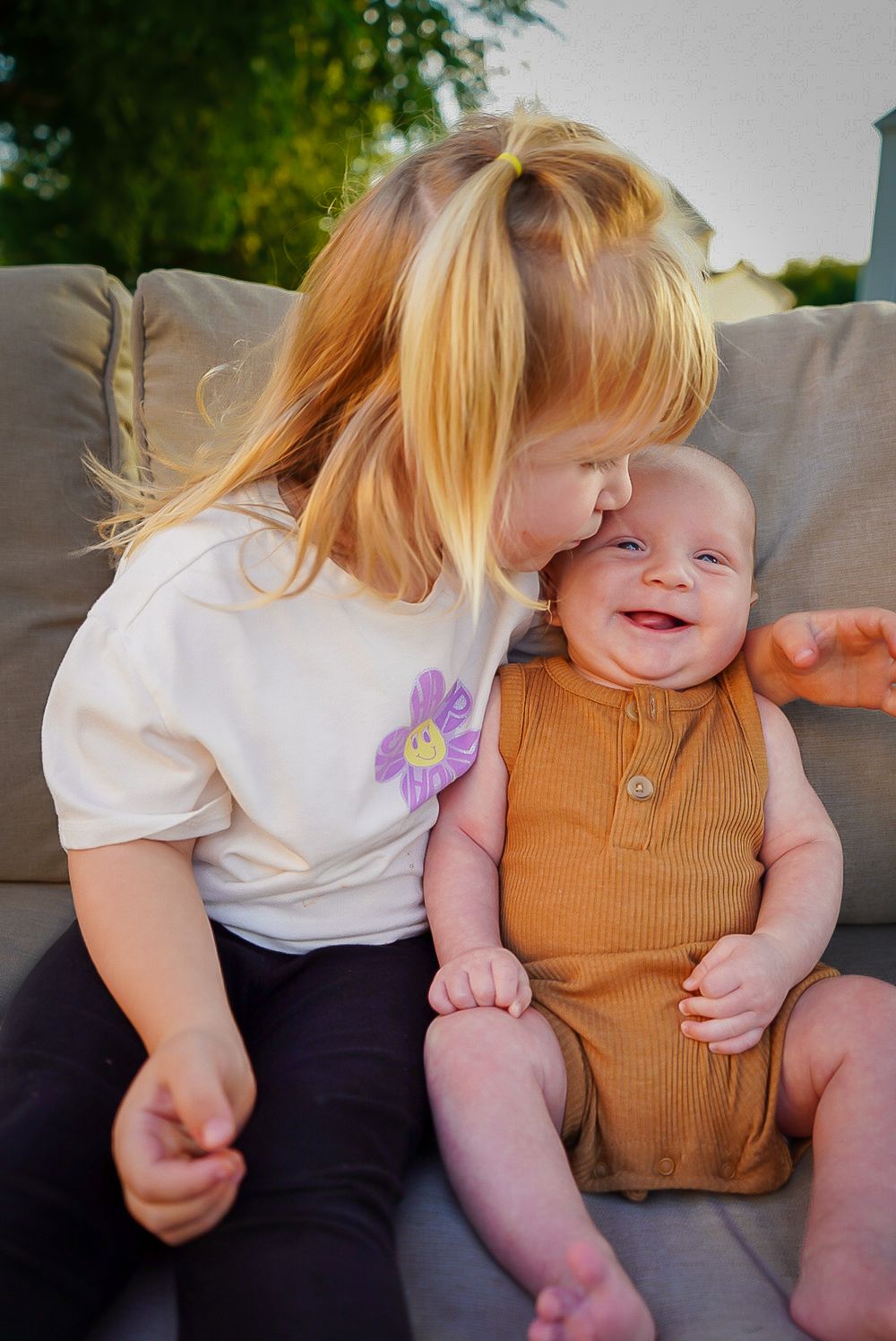 Two young children share an affectionate moment while sitting together in outdoor setting.