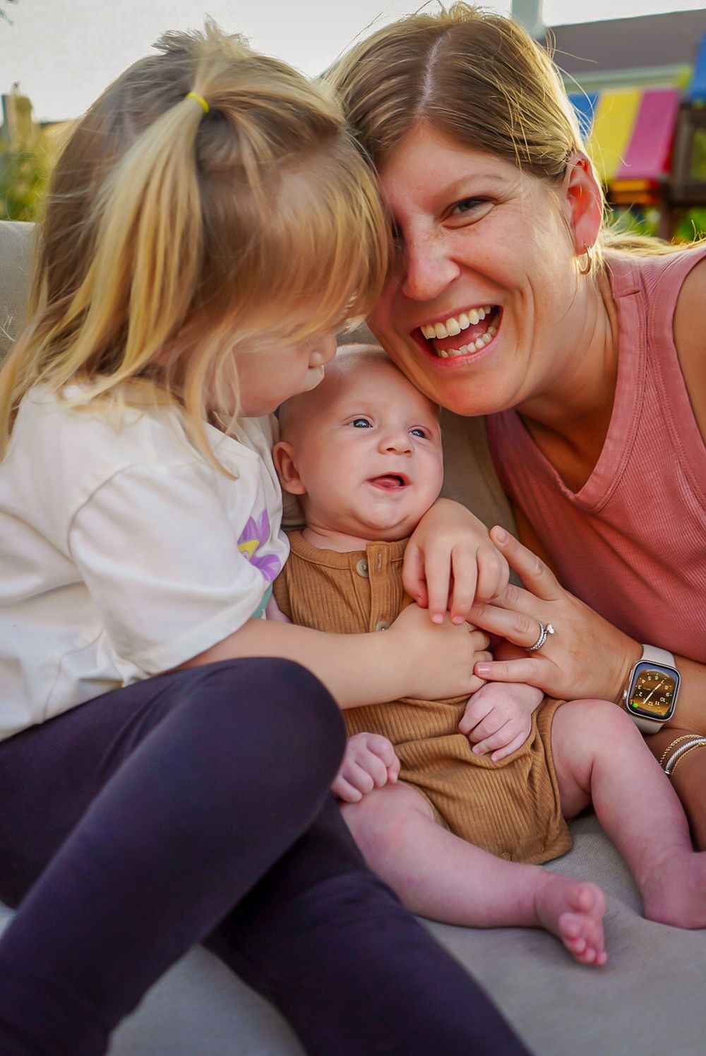 A joyful family moment captured outdoors as they laugh and cuddle together on a sunny day.