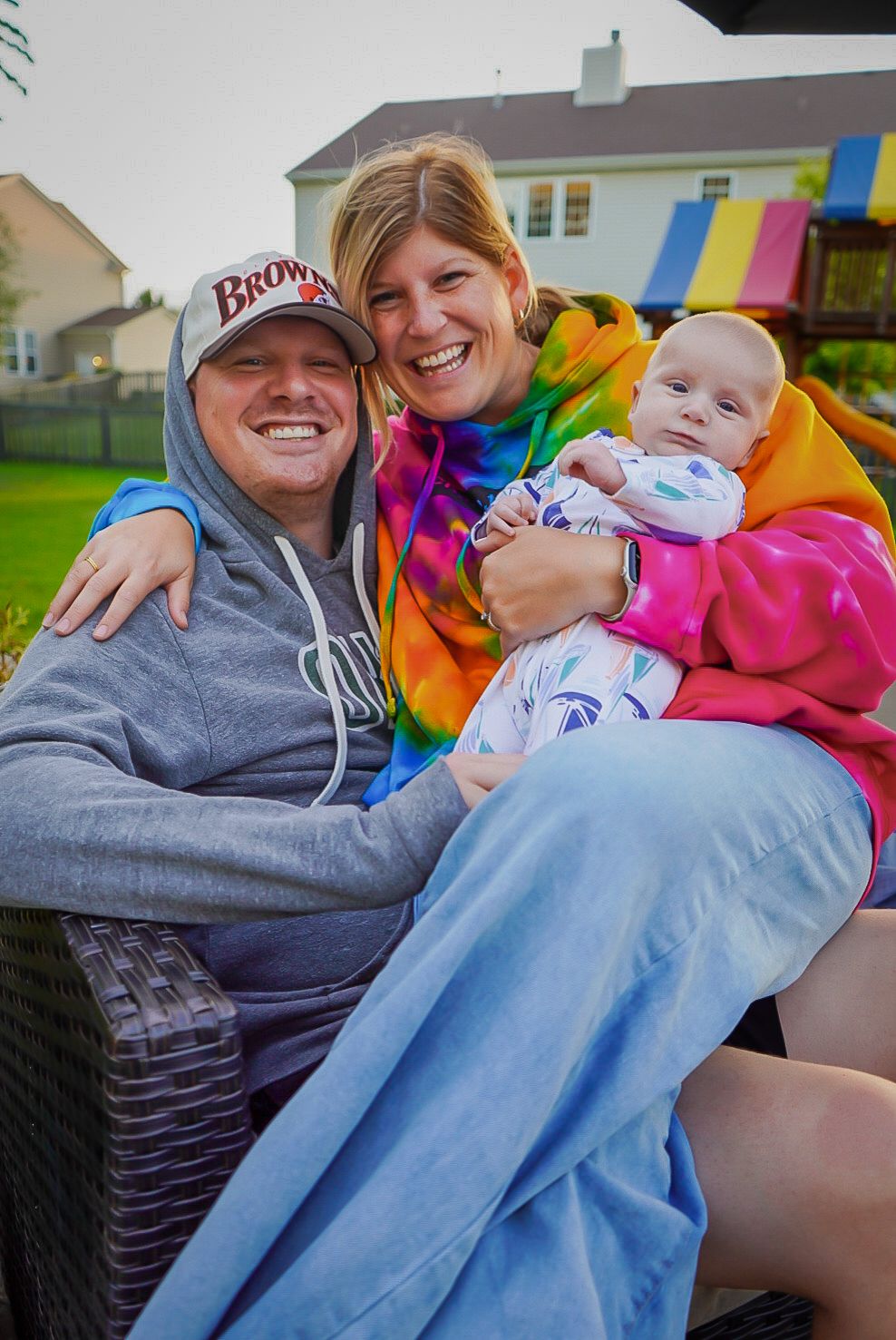 two adults and a baby smiling sitting together outdoors on a sunny day