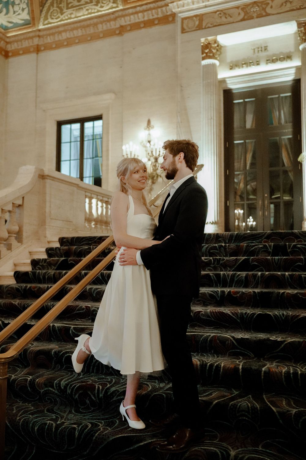 A couple dances together in an elegant ballroom with dark vintage theater seating in the background.