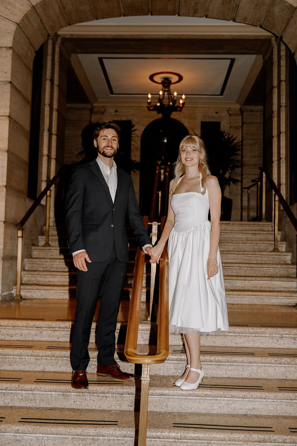 A couple in formal wear descending elegant marble stairs at a venue.