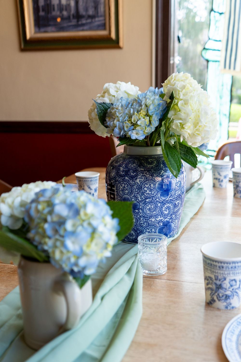 Blue and white vases filled with hydrangea flowers create an elegant table centerpiece at wedding reception with soft natural lighting.