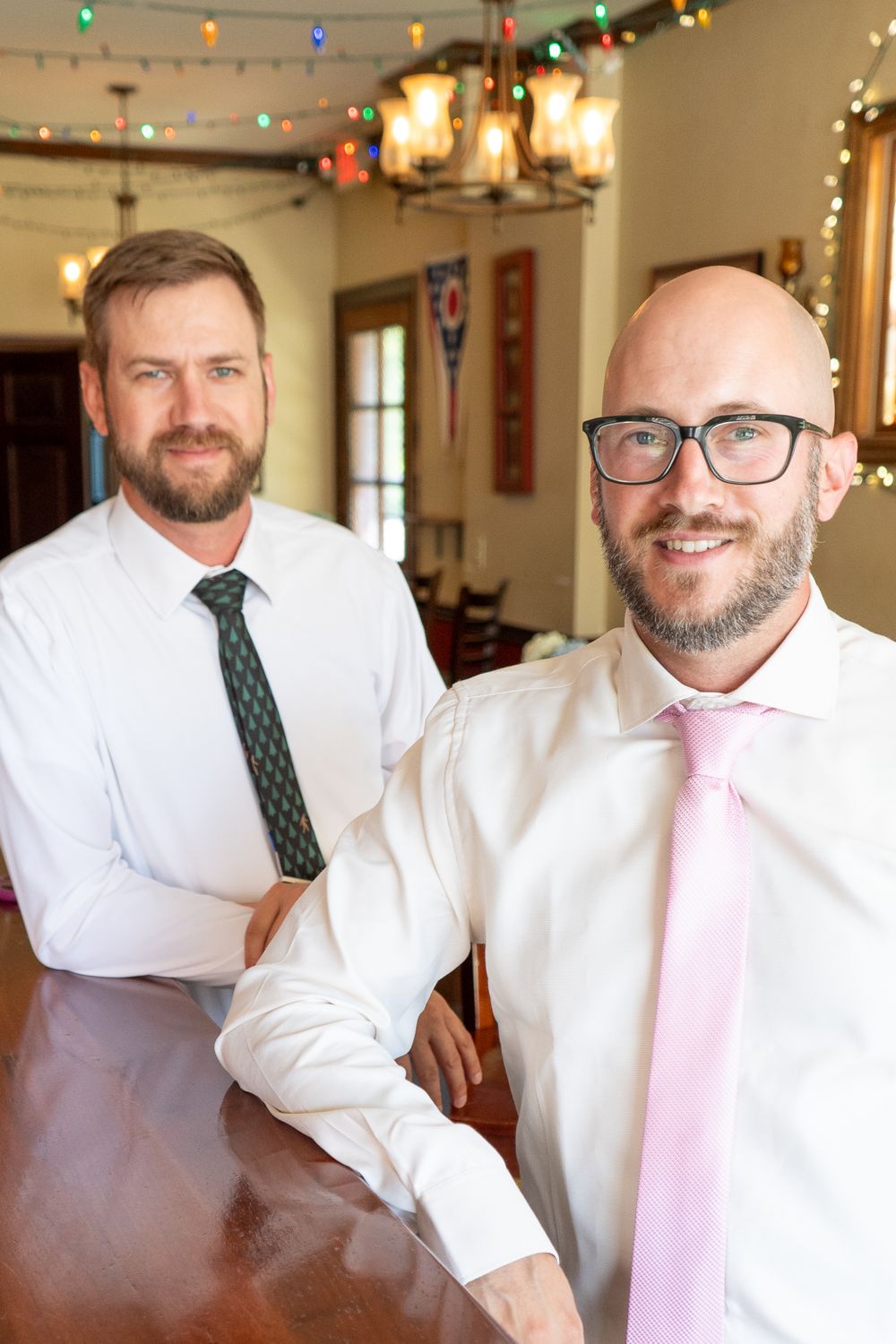 two people in white shirts and ties at a formal gathering with party lights.