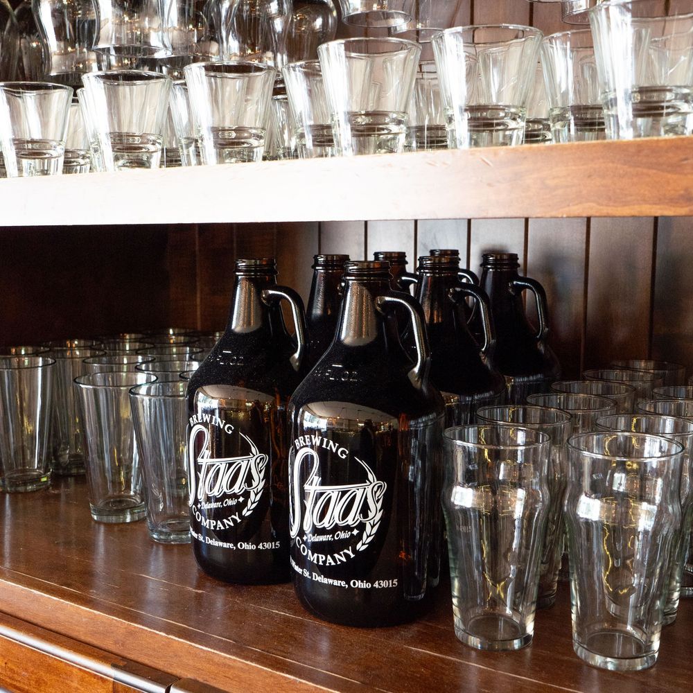 Glass beer mugs and bottles stored on wooden shelves in a bar or restaurant setting.