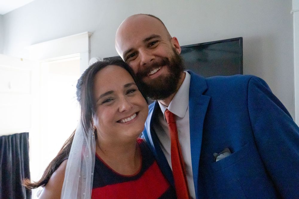 two people in formal wedding attire, with the guest wearing a bright blue suit and red tie and bride.
