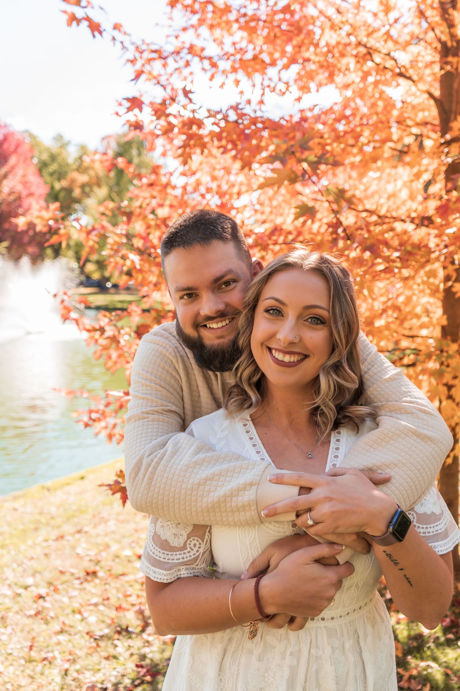 A couple shares warm embraces and laughter among vibrant orange autumn foliage by a lakeside.